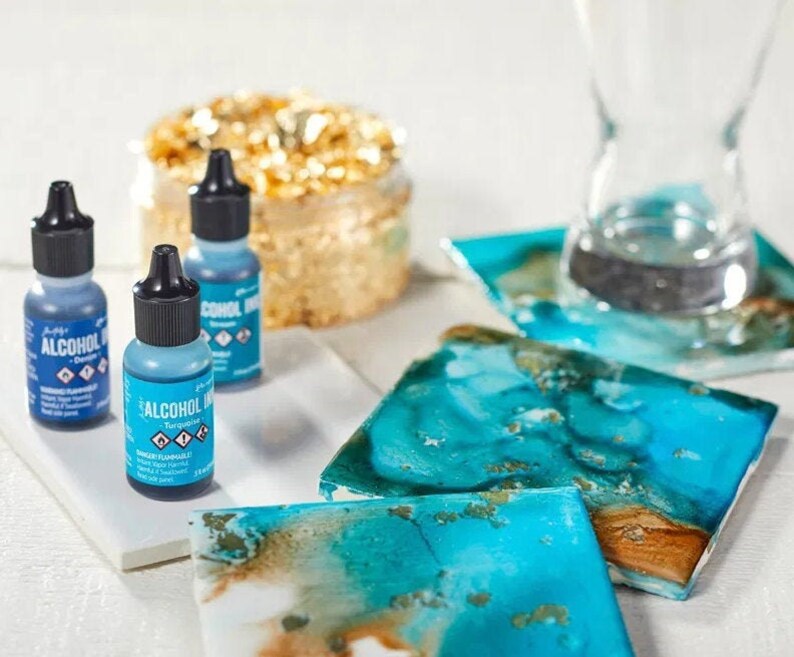 May include: Three bottles of alcohol ink in turquoise, teal, and denim blue. The bottles are labeled "Alcohol Ink" and have a dropper top. The ink is used for creating art on various surfaces, such as resin, epoxy, and alcohol inks.