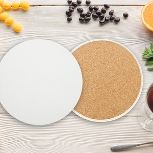 May include: Two round coasters, one white and one cork, on a white wooden surface. The white coaster is blank and the cork coaster has a natural brown colour. There are other items on the surface, including a bowl of yellow sweets, a bowl of chocolate sweets, a glass of tea, and a spoon.