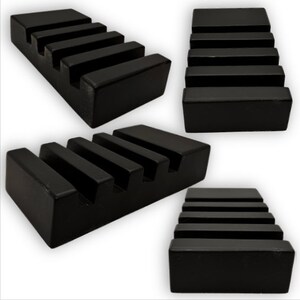 May include: Four views of a black, rectangular soap dish with a stepped design. The dish has five horizontal grooves, creating a tiered appearance. The soap dish is made of a solid, matte black material.