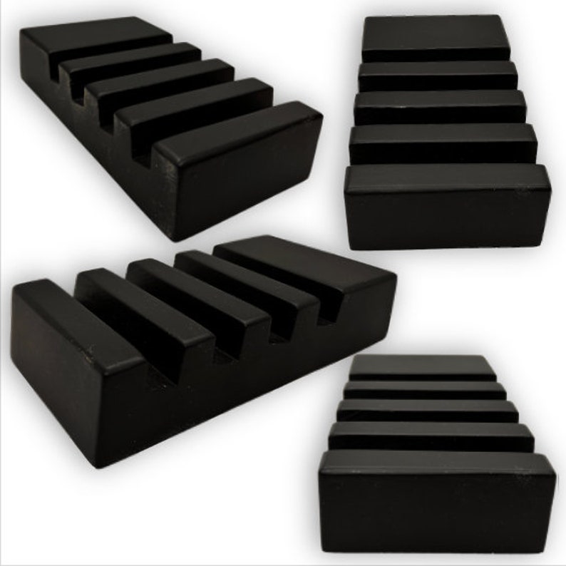 May include: Four views of a black, rectangular soap dish with a stepped design. The dish has five horizontal grooves, creating a tiered appearance. The soap dish is made of a solid, matte black material.