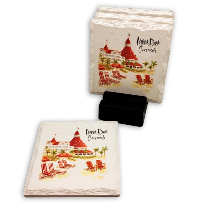 May include: Set of four square stone coasters with a watercolor painting of the Hotel Del Coronado. The image includes the hotel, beach chairs, and palm trees. The coasters are displayed in a black holder.