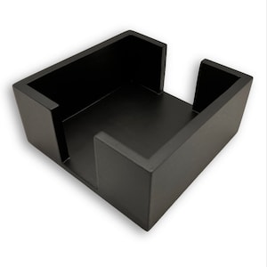 May include: Black wooden desk organizer with a square base and a rectangular opening in the center. The organizer is designed to hold notepads, pens, or other office supplies.