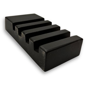 May include: A solid black wooden soap dish with a stepped design. The dish has four parallel grooves for drainage and a rectangular shape. The finish is matte, and the wood grain is visible.