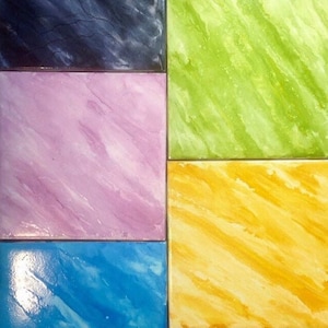 May include: A close-up of four square tiles with different marbled patterns. The tiles are painted in shades of blue, green, yellow, and pink.