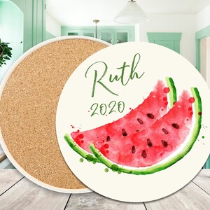 May include: Round cork and ceramic coaster with a white background and a watercolour illustration of a watermelon slice. The text "Ruth 2020" is printed on the coaster.