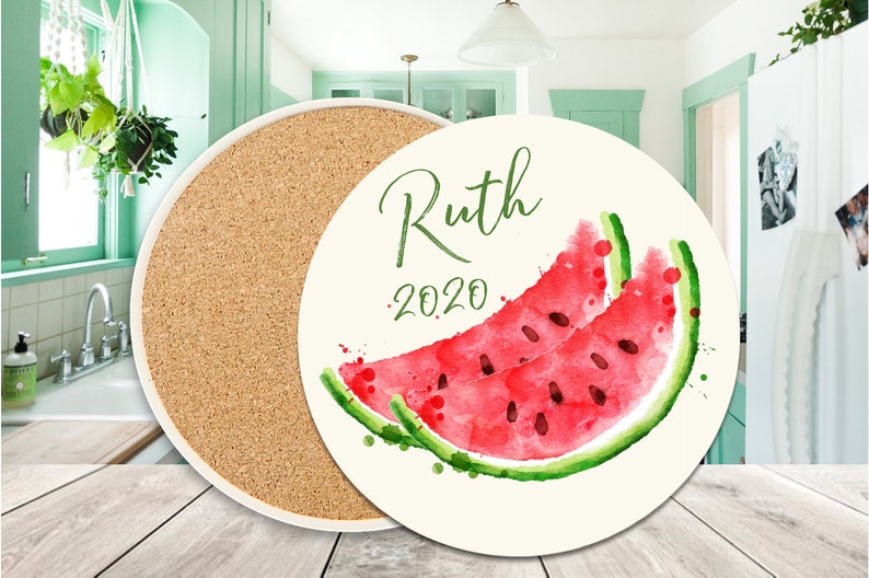 May include: Round cork and ceramic coaster with a white background and a watercolour illustration of a watermelon slice. The text "Ruth 2020" is printed on the coaster.