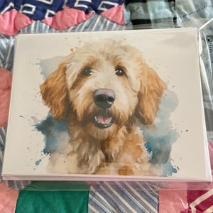 May include: A watercolor painting of a light brown dog with a white chest and a happy expression. The dog is surrounded by blue and white watercolor splatters.