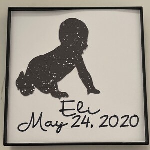 May include: A black silhouette of a baby crawling with a starry pattern. The name Eli and the date May 24, 2020 are written below the silhouette.