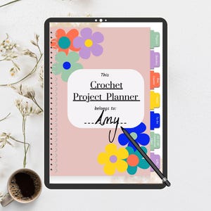 May include: A pink digital planner with the text "This Crochet Project Planner belongs to: Amy" on the cover. The cover is decorated with colorful flowers and has tabs on the right side.