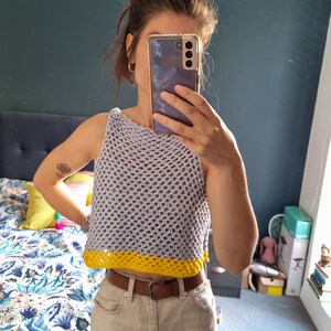 May include: A gray crochet top with a yellow trim. The top is sleeveless and has a loose fit.