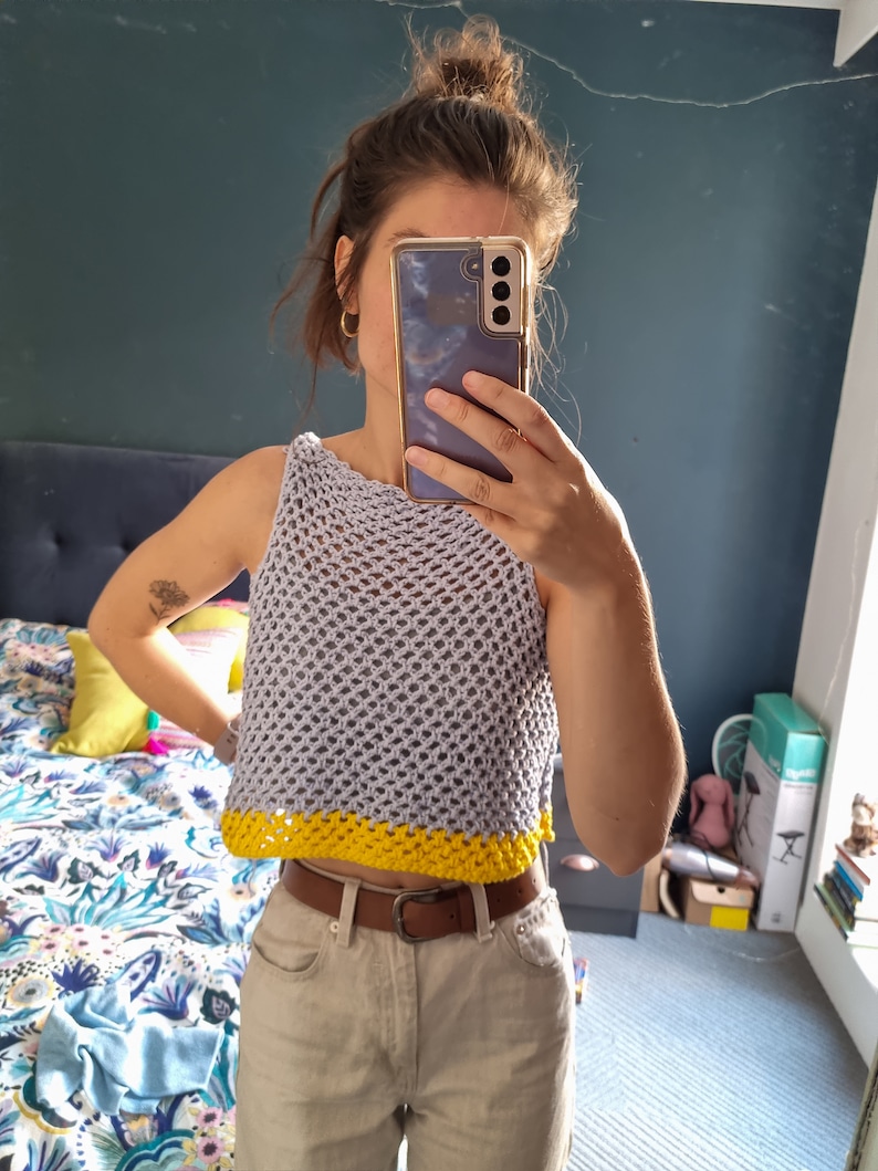 May include: A gray crochet top with a yellow trim. The top is sleeveless and has a loose fit.