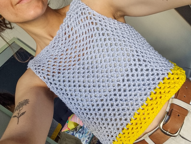 May include: A light blue crochet top with a yellow crocheted trim. The top is sleeveless and has a loose fit.