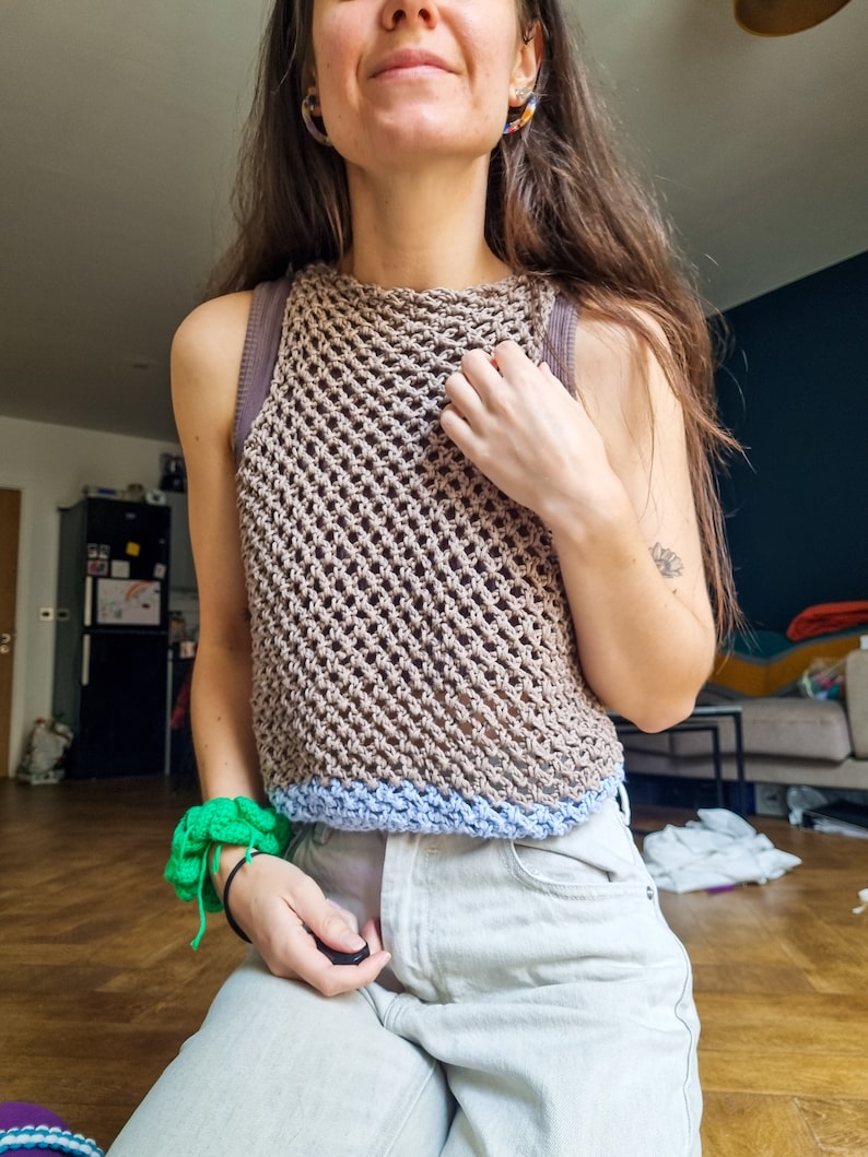 May include: A brown crochet tank top with a light blue trim. The top is made with a loose, open stitch pattern.