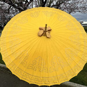 May include: A yellow umbrella with a gold trim and intricate designs. The umbrella is open and the top is visible.