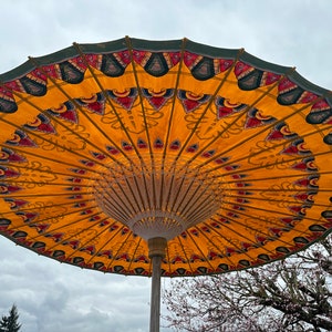 May include: A large, yellow and green umbrella with intricate patterns. The umbrella is open and the underside is visible. The umbrella is made of fabric and has a wooden frame.