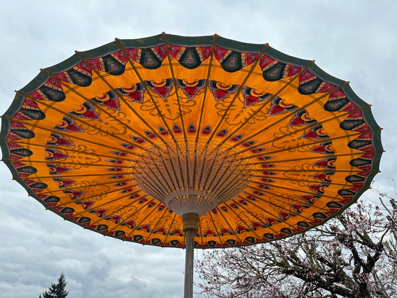 May include: A large, yellow and green umbrella with intricate patterns. The umbrella is open and the underside is visible. The umbrella is made of fabric and has a wooden frame.