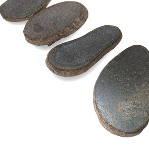 May include: Four irregular, flat, dark gray stones with textured, brown, porous edges arranged in a diagonal line. Each stone features a smooth, polished top surface with subtle speckling and a distinct, rough, natural-looking outer rim.