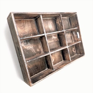 May include: A rectangular wooden tray with a dark, distressed brown finish and visible wood grain. The tray features nine individual compartments separated by fixed dividers and includes two integrated cutout handles on the side panels.