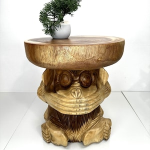 May include: A wooden monkey stool with a round top. The stool is carved with a monkey face and has a natural wood finish.