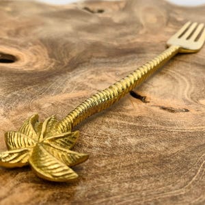 May include: A gold palm tree fork with a twisted handle. The fork is on a wooden surface.