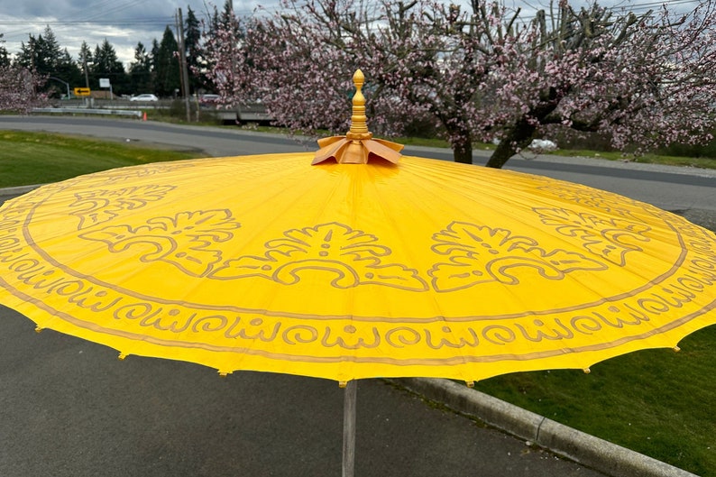 May include: A yellow and gold umbrella with a decorative design. The umbrella has a pointed top and a circular canopy.