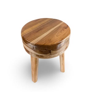 May include: A small, round wooden stool with a natural finish. The stool has a circular seat and three short, sturdy legs. The wood grain is visible, showcasing the natural color variations of the wood. The stool is approximately 12 inches in height.