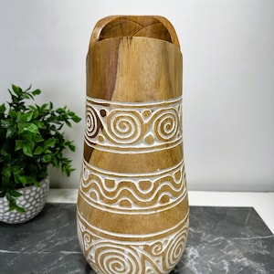May include: A wooden vase with a carved design in white. The vase is brown and has a wide opening at the top.