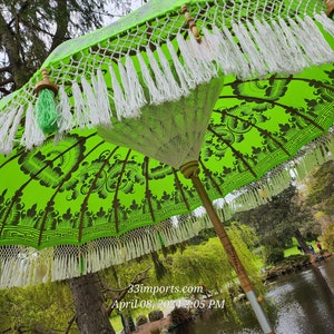 Pu&ograve; includere: Un ombrello verde e bianco con frange bianche e nappe verdi. L'ombrello &egrave; aperto e la parte superiore &egrave; visibile. L'ombrello &egrave; in un giardino con alberi e uno stagno sullo sfondo.