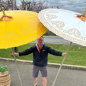 May include: Two large, decorative umbrellas with gold trim and ornate patterns. The umbrella on the left is yellow, and the umbrella on the right is white.