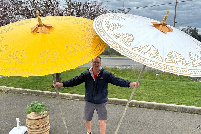 May include: Two large, decorative umbrellas with gold trim and ornate patterns. The umbrella on the left is yellow, and the umbrella on the right is white.