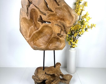 May include: A large, abstract sculpture made from natural wood with a unique, organic shape. The sculpture is mounted on a smaller wooden base and features two black metal rods for support.
