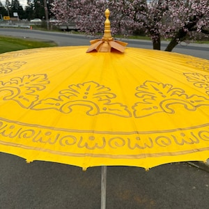 May include: A yellow umbrella with a gold trim and intricate floral designs. The umbrella has a wooden handle with a gold finial.