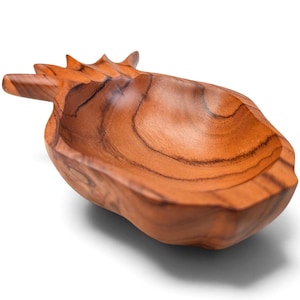 May include: A carved wooden bowl shaped like a pineapple, featuring a warm brown color with visible natural wood grain patterns. The bowl has a smooth, concave interior and a textured exterior that mimics the form of a pineapple fruit.