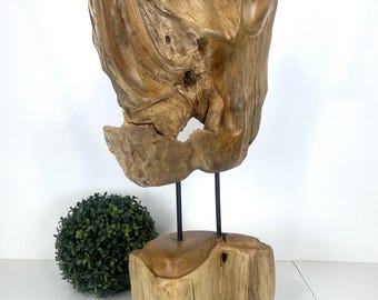 May include: A natural wood sculpture with a unique, abstract shape. The sculpture is made of light brown wood and is mounted on a wooden base with two black metal rods.