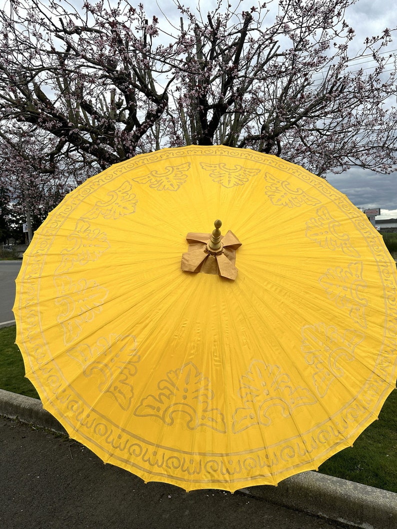 May include: A yellow umbrella with a gold trim and intricate designs. The umbrella is open and the top is visible.