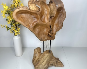 May include: A large, natural, brown, wooden sculpture with a unique, abstract shape. The sculpture is mounted on a smaller, natural, brown, wooden base with two black metal rods.
