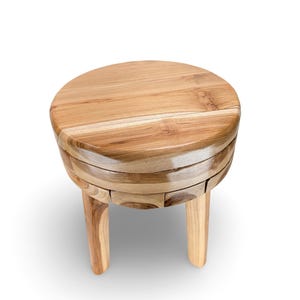 May include: A round wooden stool featuring a smooth, polished top with visible natural grain patterns. The stool is constructed from multiple segments of light brown wood, supported by three sturdy, cylindrical legs that extend downward.