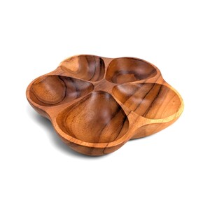 May include: A brown wooden serving dish featuring a flower-like shape with five distinct, rounded compartments. The natural wood grain is visible throughout the surface, showcasing varied light and dark brown tones across the smooth, curved sections.