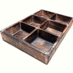 May include: A rectangular wooden tray featuring a dark brown, distressed finish with visible wood grain. The tray is divided into six individual compartments of varying sizes, separated by fixed wooden dividers, creating a structured storage organizer.