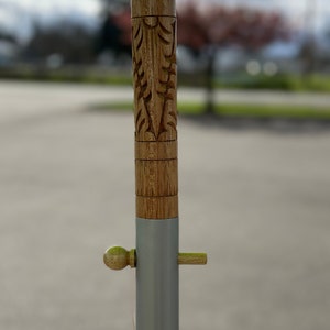 Pu&ograve; includere: Un palo di legno con un design intagliato e una fascia di metallo argentato. Il palo ha un piccolo pomo di legno e uno spillo di metallo.