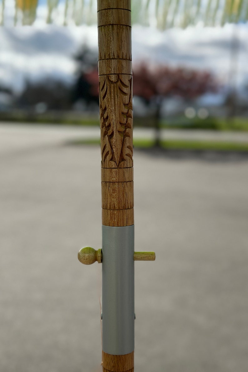 Pu&ograve; includere: Un palo di legno con un design intagliato e una fascia di metallo argentato. Il palo ha un piccolo pomo di legno e uno spillo di metallo.