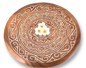 May include: A round wooden serving tray with a carved geometric design in a light brown color. The tray has a white flower in the center.