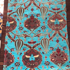 Può includere: Un tessuto turchese con un motivo ripetitivo di fiori e foglie stilizzati in tonalità di rosso, marrone e oro.