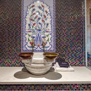 Puede incluir: Un lavabo de mármol blanco con dos cuencos pequeños a cada lado. El lavabo está decorado con intrincados diseños florales y está colocado contra una pared de azulejos de mosaico.