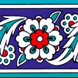 Op de afbeelding: Decoratieve keramische tegel met een herhalend bloemmotief. Het ontwerp toont witte bloemen met rode centra en turquoise accenten tegen een diepblauwe achtergrond. De rand wordt omlijnd door witte en turquoise lijnen.