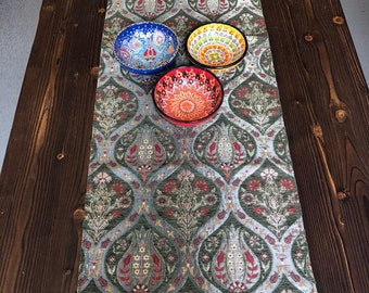 Könnte beinhalten: Ein grüner und silberner Tischläufer mit einem floralen Muster und goldenen Fransen. Drei bunte Keramik Schalen sind auf dem Läufer platziert.