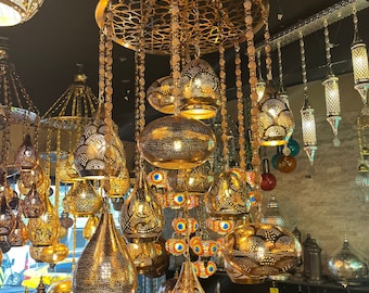 Könnte beinhalten: Ein goldfarbener Kronleuchter mit mehreren hängenden Lichtern. Die Leuchten sind aus Metall und haben ein dekoratives, filigranes Design. Der Kronleuchter hängt von der Decke und ist von anderen Lichtern umgeben.