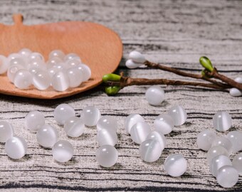 May include: A collection of white cat's eye beads, some are in a wooden bowl and others are scattered on a textured surface.