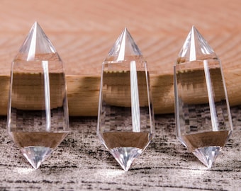 May include: Three clear crystal points, each with a pointed tip and a flat base, are arranged in a row on a wooden surface.