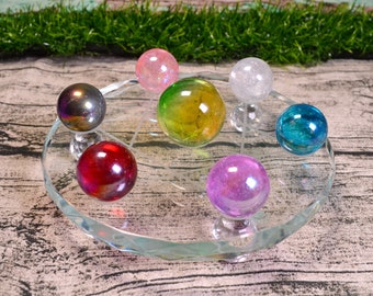 May include: A set of seven iridescent crystal spheres on a clear glass stand. The spheres are arranged in a circle and are in various colors, including pink, green, blue, red, and purple.